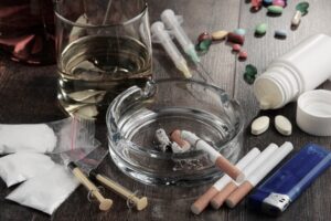 Glass of alcohol with different drugs and paraphernalia on a wooden table 